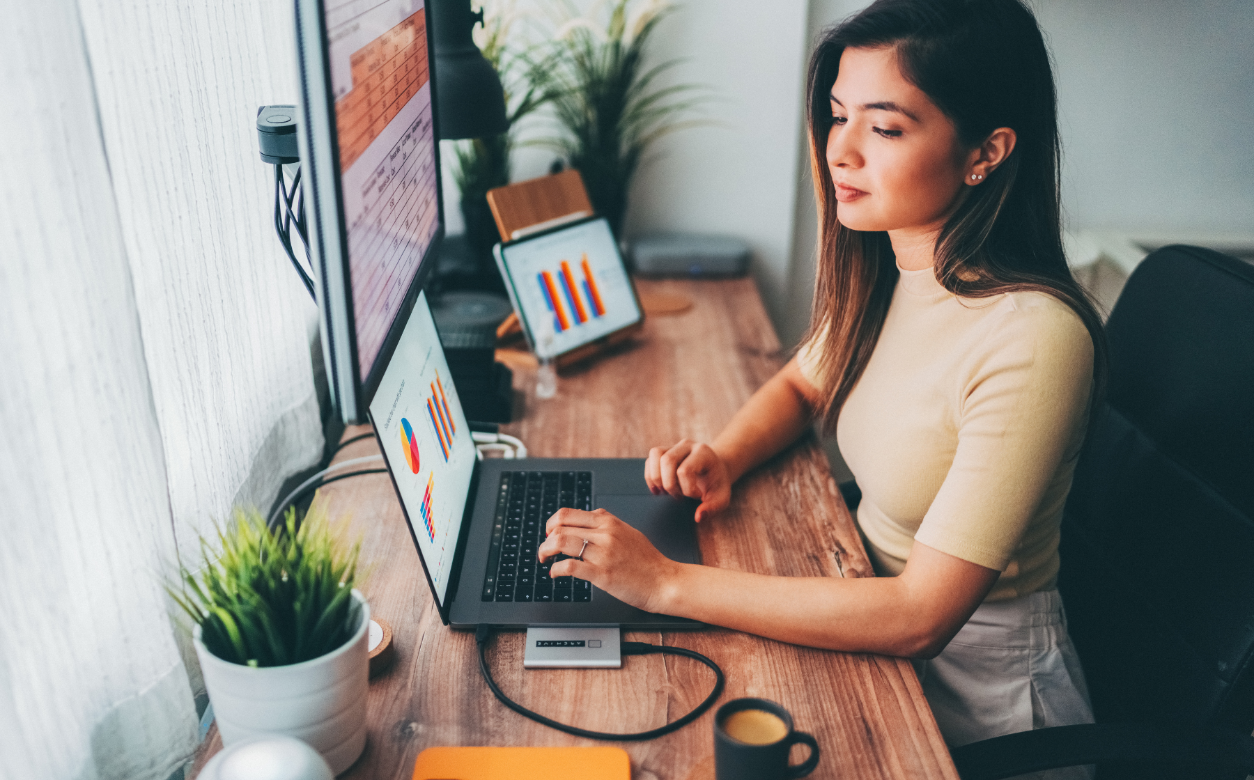 Woman working remotely at desk with charts and graphs on screen