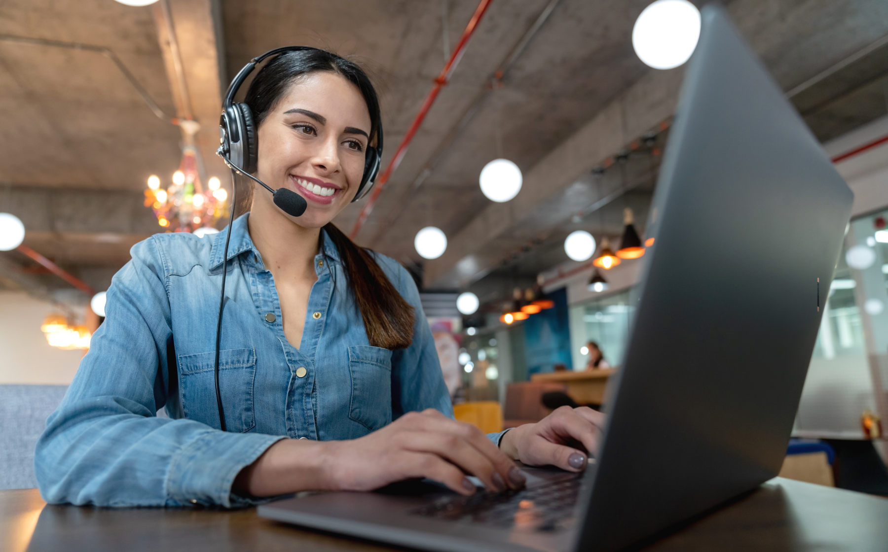 Smiling woman in headset working on laptop in a modern office space