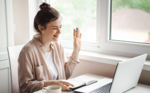 Woman smiling and waving a pen during a video call at her desk