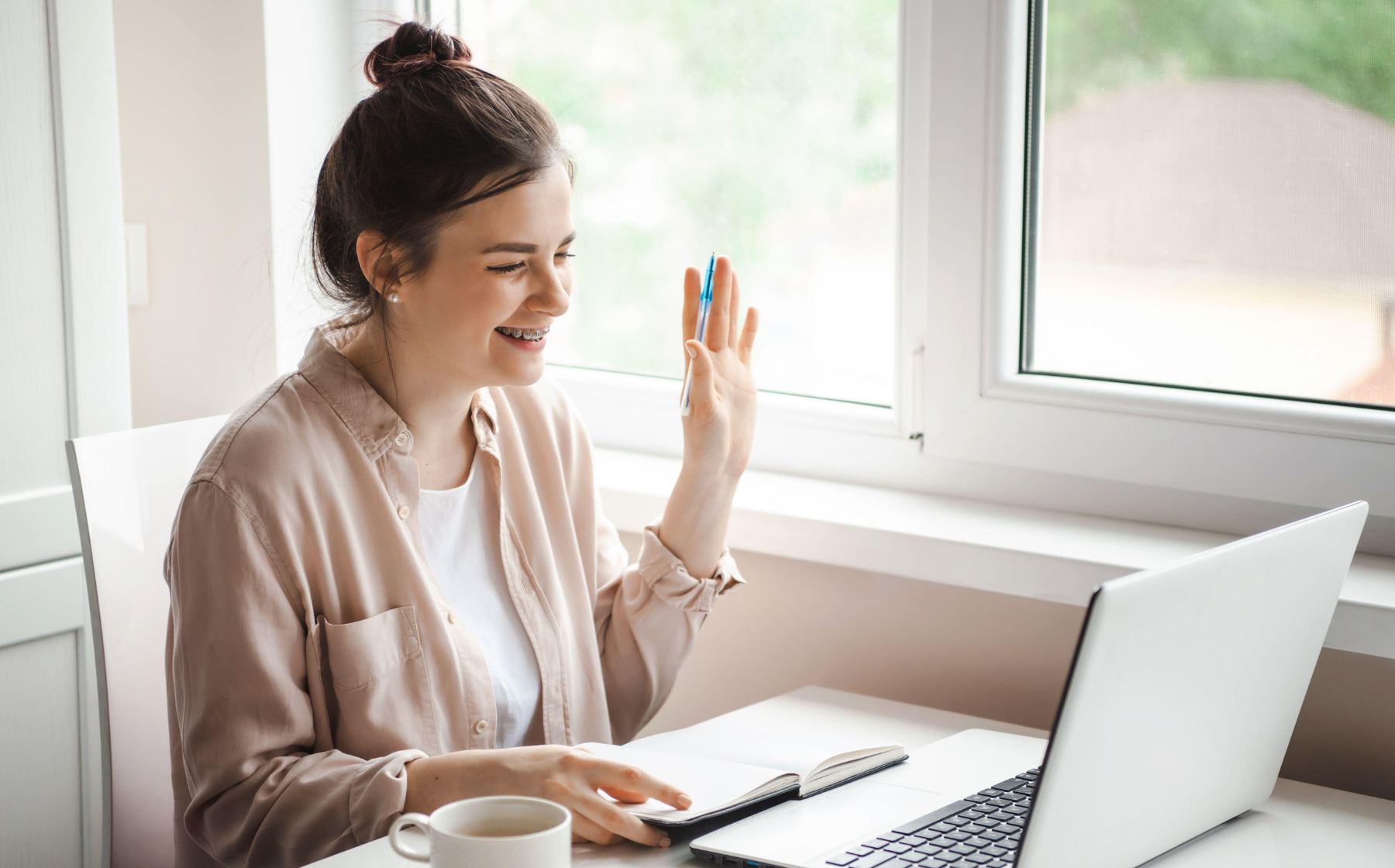 Woman smiling and waving a pen during a video call at her desk