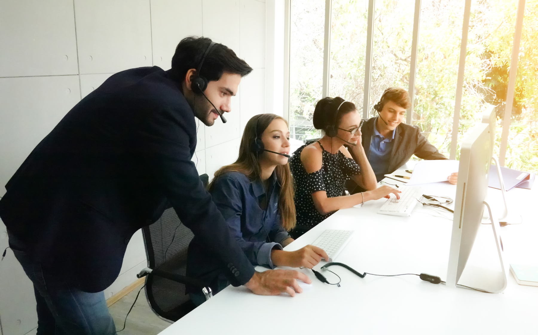 Team wearing headsets working at computers in an office with a supervisor assisting.