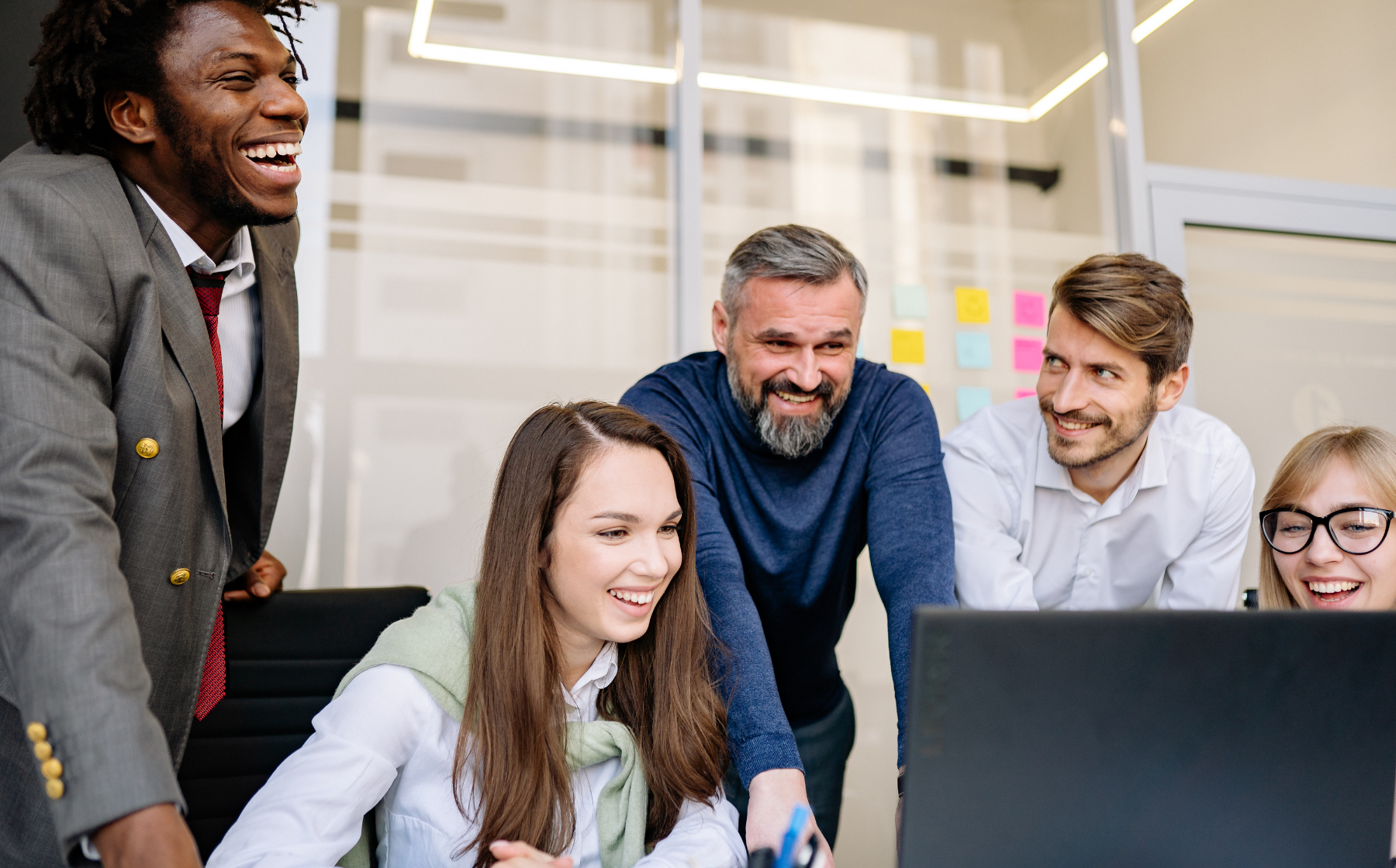 Colleagues gathered around a computer, smiling during a meeting