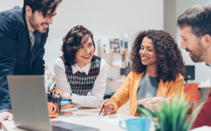 Four coworkers smile and collaborate around a laptop in an office