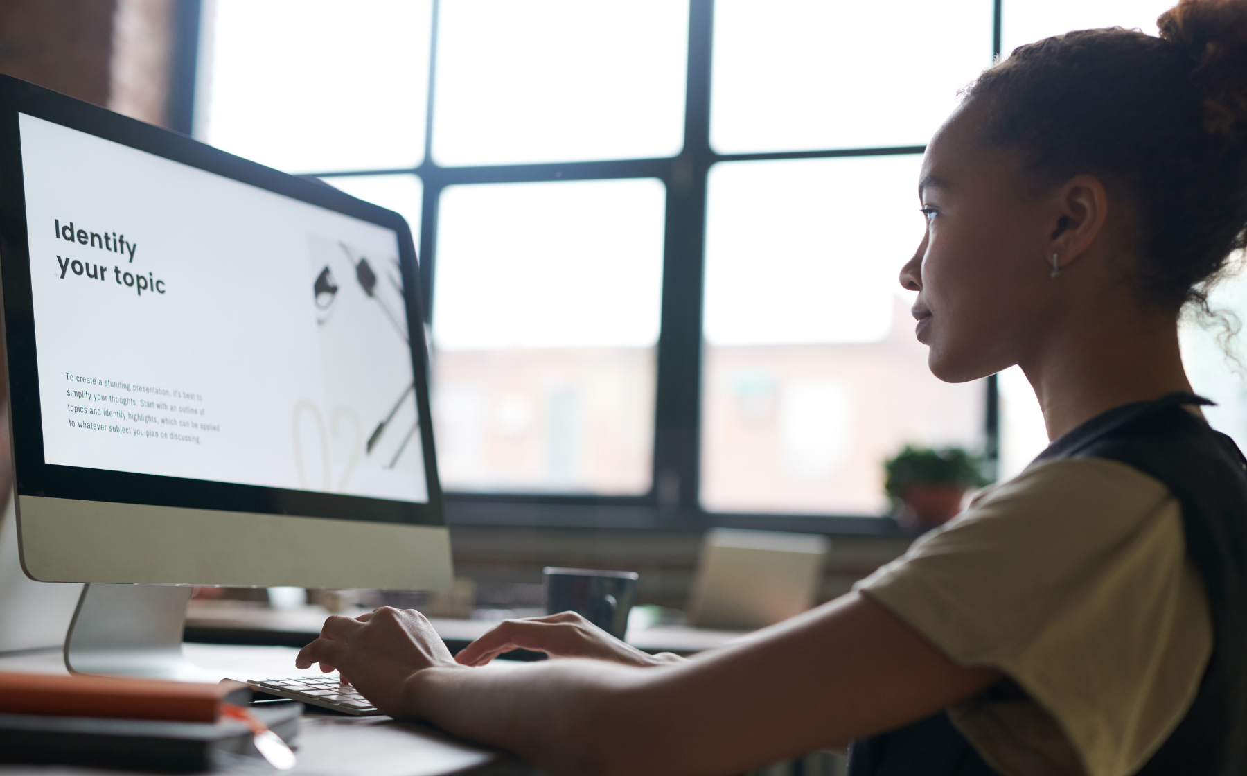 A woman works at a desktop computer displaying a presentation prompt