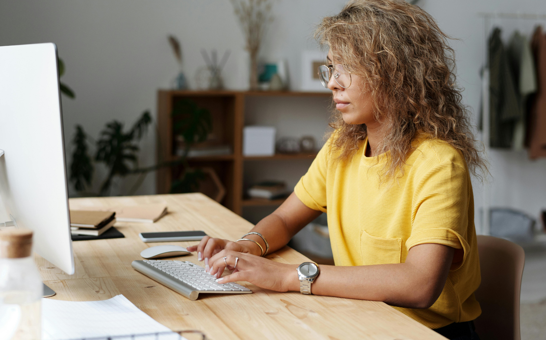 Woman in a yellow shirt types at a computer in a home office